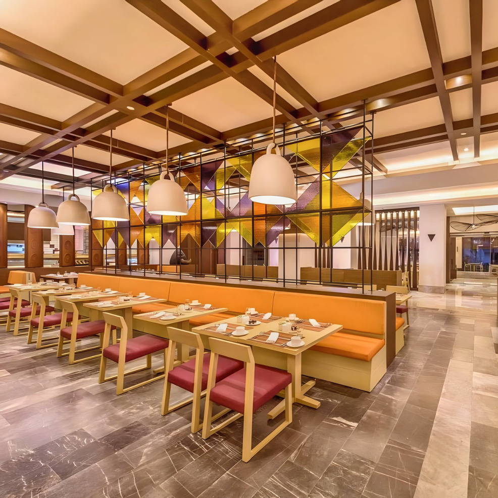 Interior of a modern restaurant, a perfect destination wedding venue with warm lighting, geometric ceiling designs, colorful booth seating, and pendant lights.