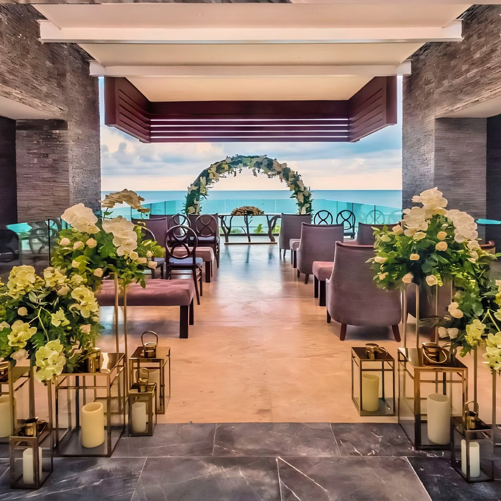 Elegant destination wedding dining area with floral decorations and a view of the ocean through an archway.