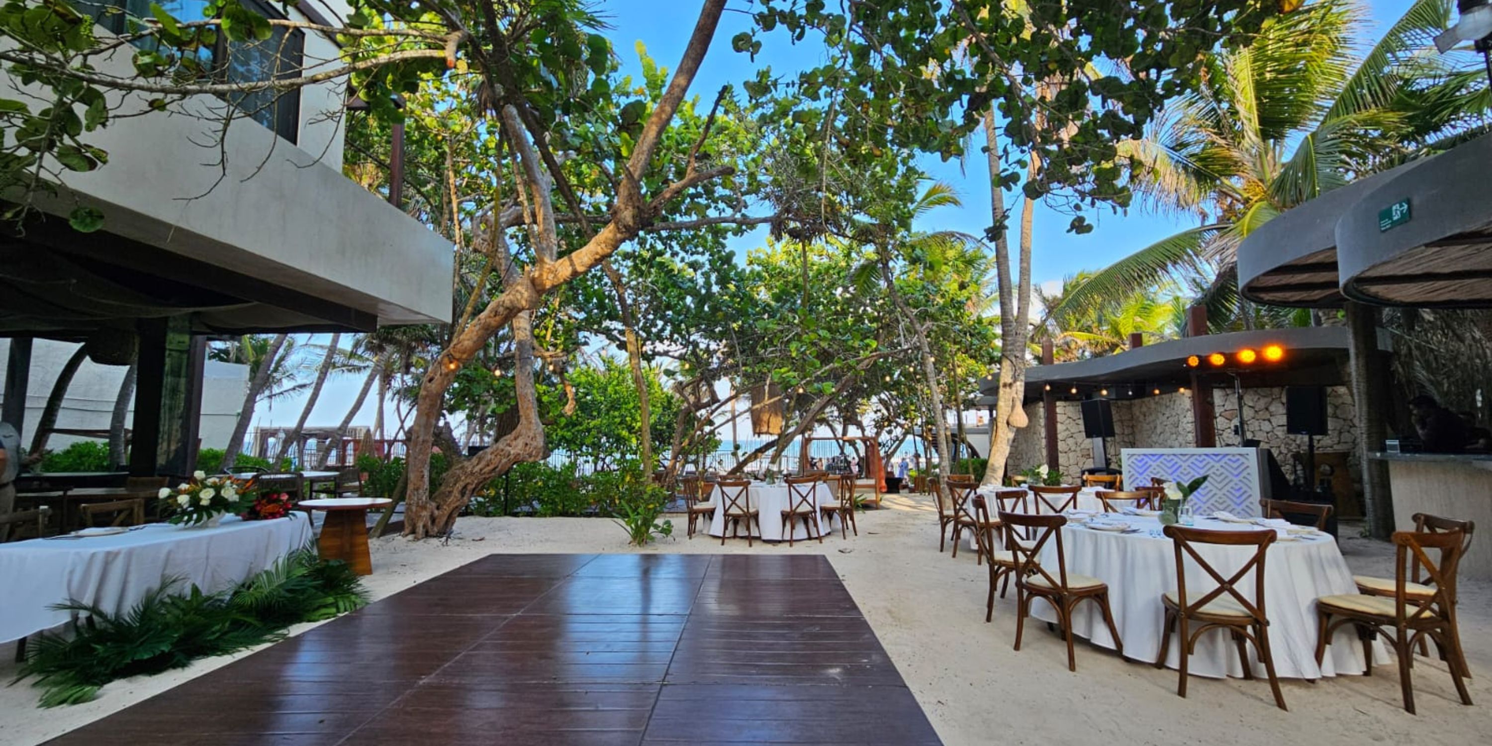 Outdoor wedding dining setup at Secrets Tulum, with round tables on sand beneath lush tropical trees.
