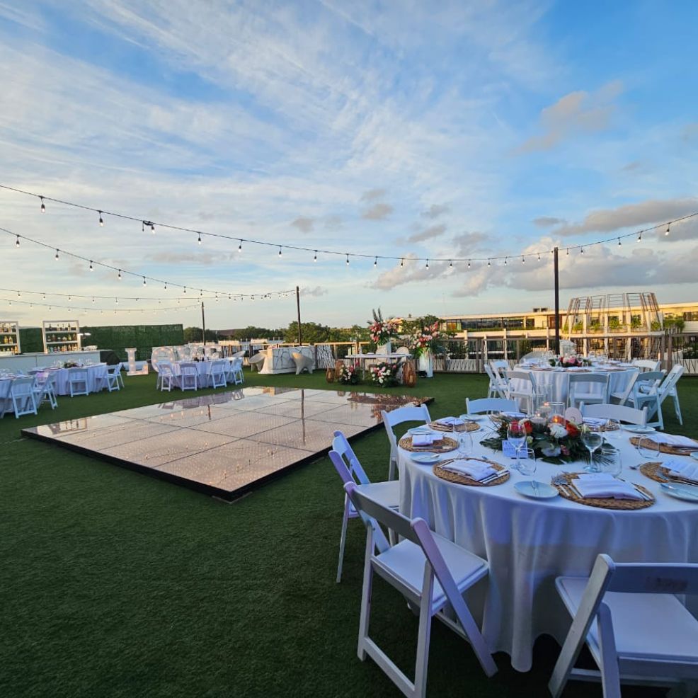 Destination wedding scene featuring round tables, white chairs, dance floor, and string lights overhead.
