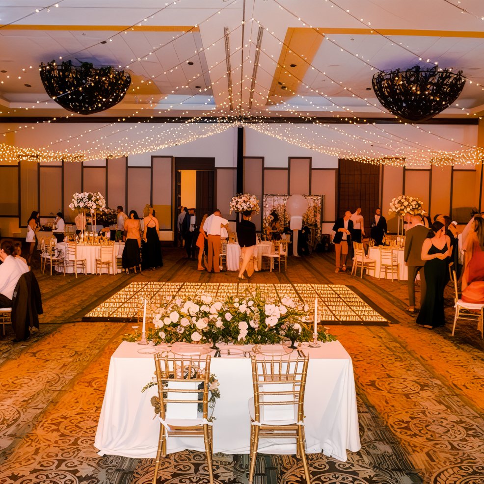 Ballroom decorated for a destination wedding with elegant tables, floral centerpieces, and string lights.