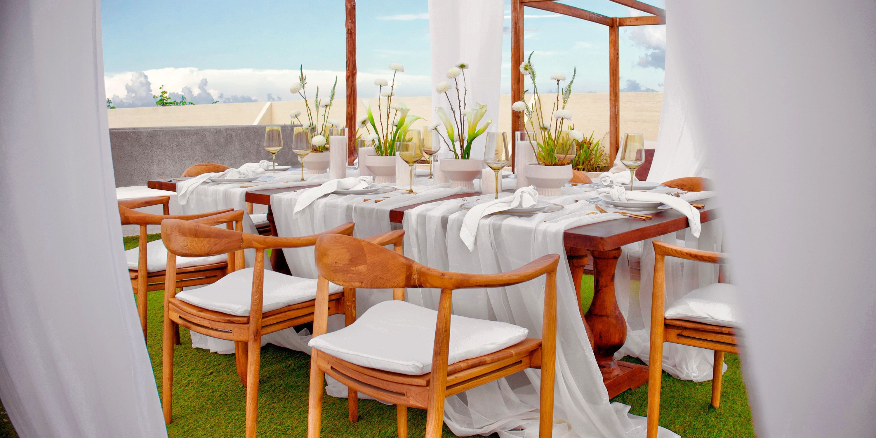 Secrets Tulum: Outdoor wedding table setup with wooden chairs, white linens, and potted plants.