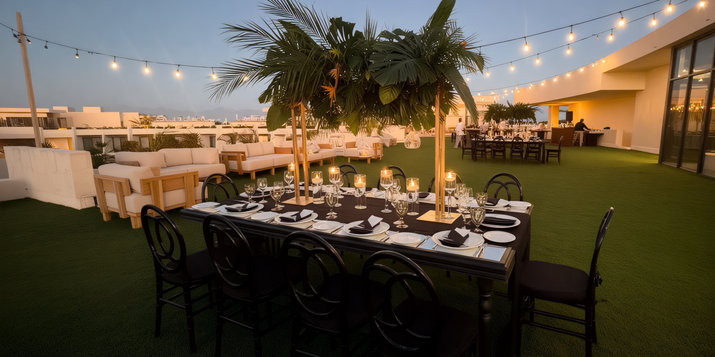 Secrets Tulum rooftop offers an enchanting setting for a destination wedding, featuring tables and chairs nestled among palm trees and illuminated by string lights at dusk.