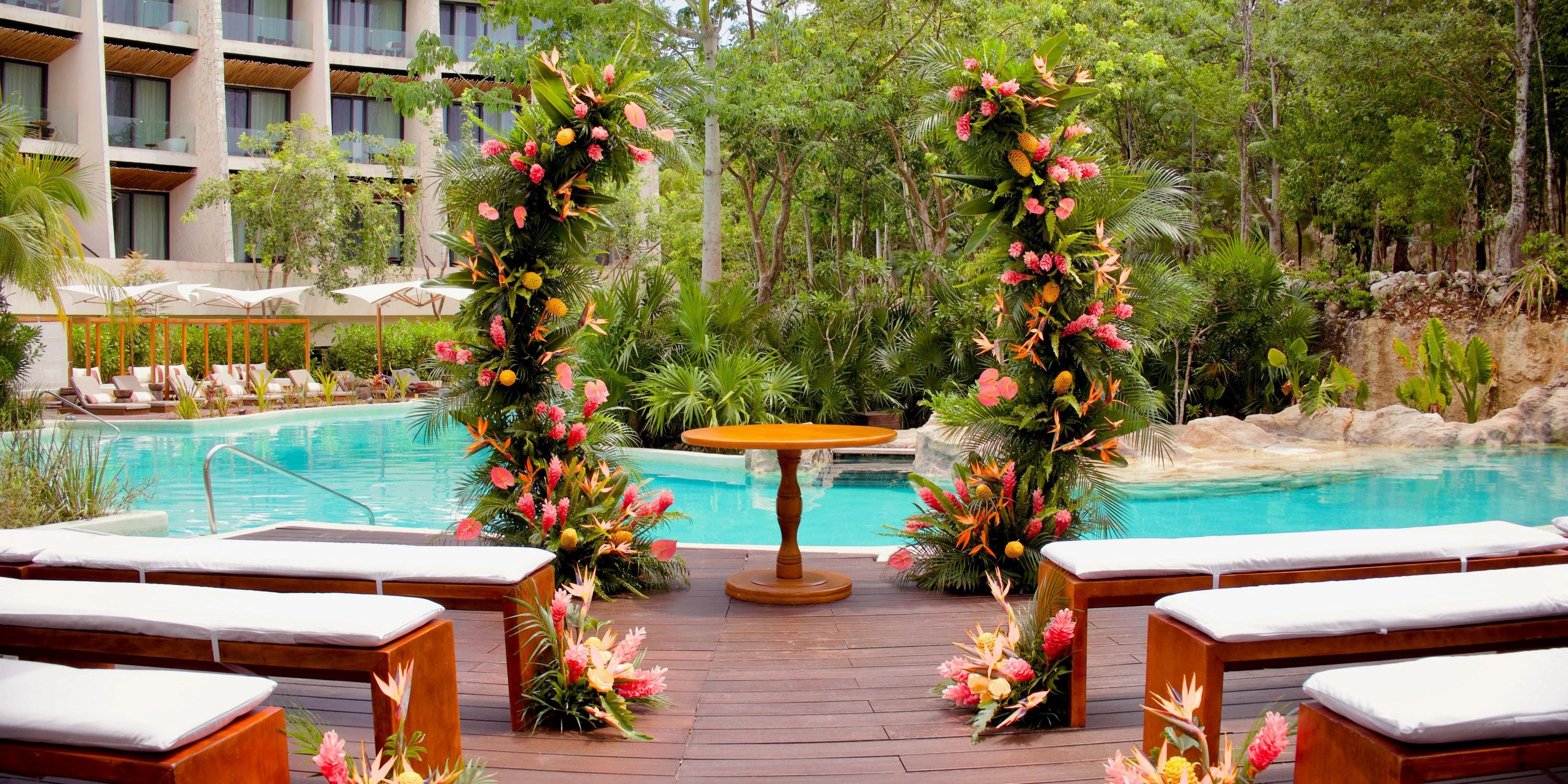 Destination wedding at Secrets Tulum by the pool, featuring floral arches and rows of white benches.