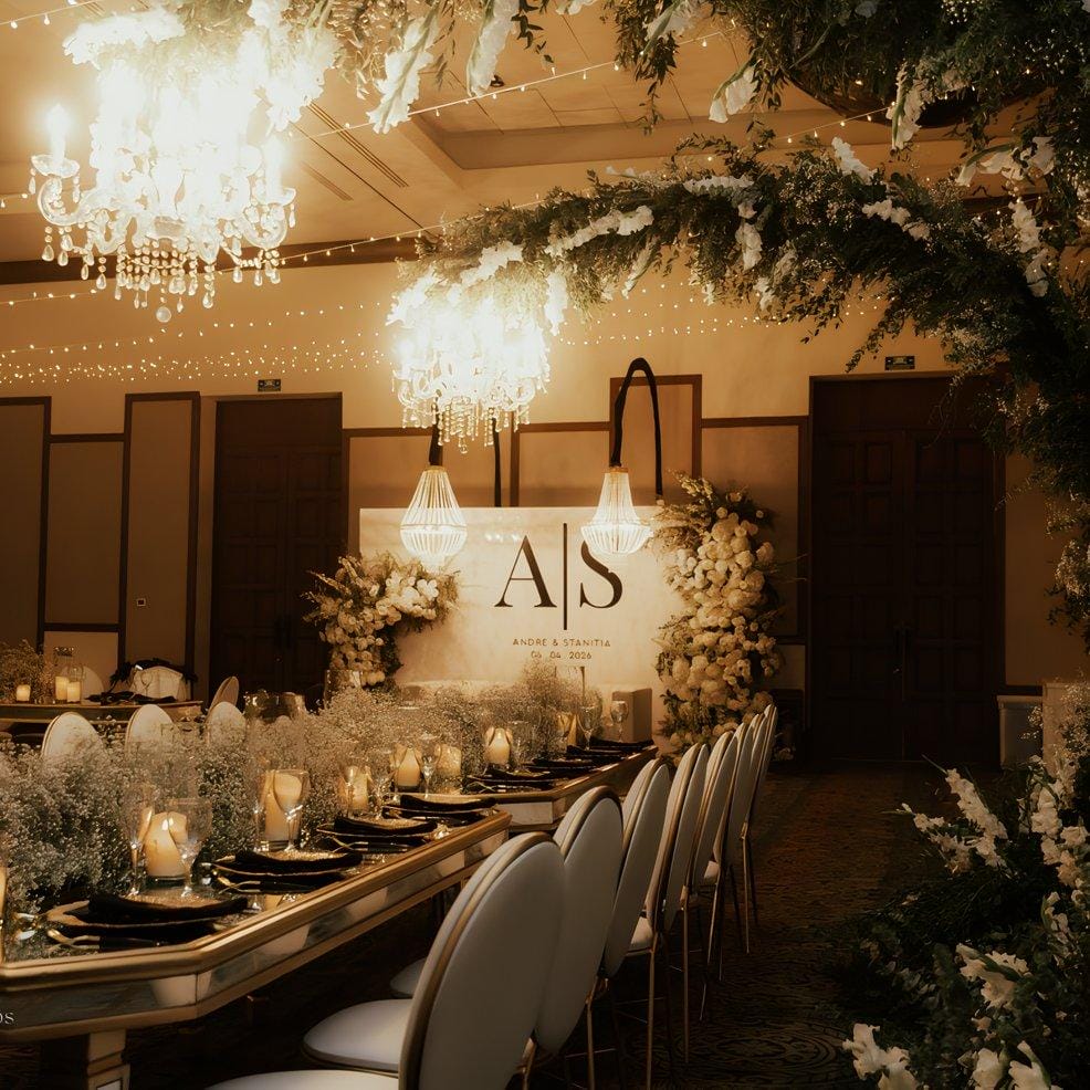 Chic wedding banquet table beneath chandeliers, adorned with flowers and candlelight decor.