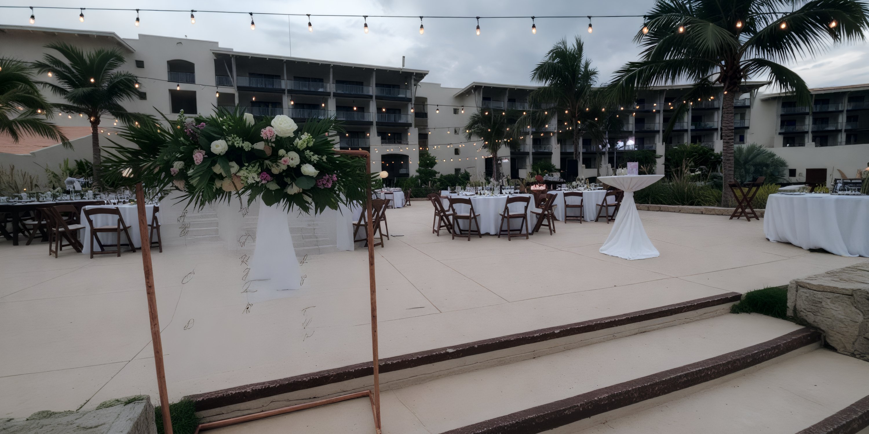 Destination wedding reception outdoors featuring round tables, string lights, and elegant floral decor.