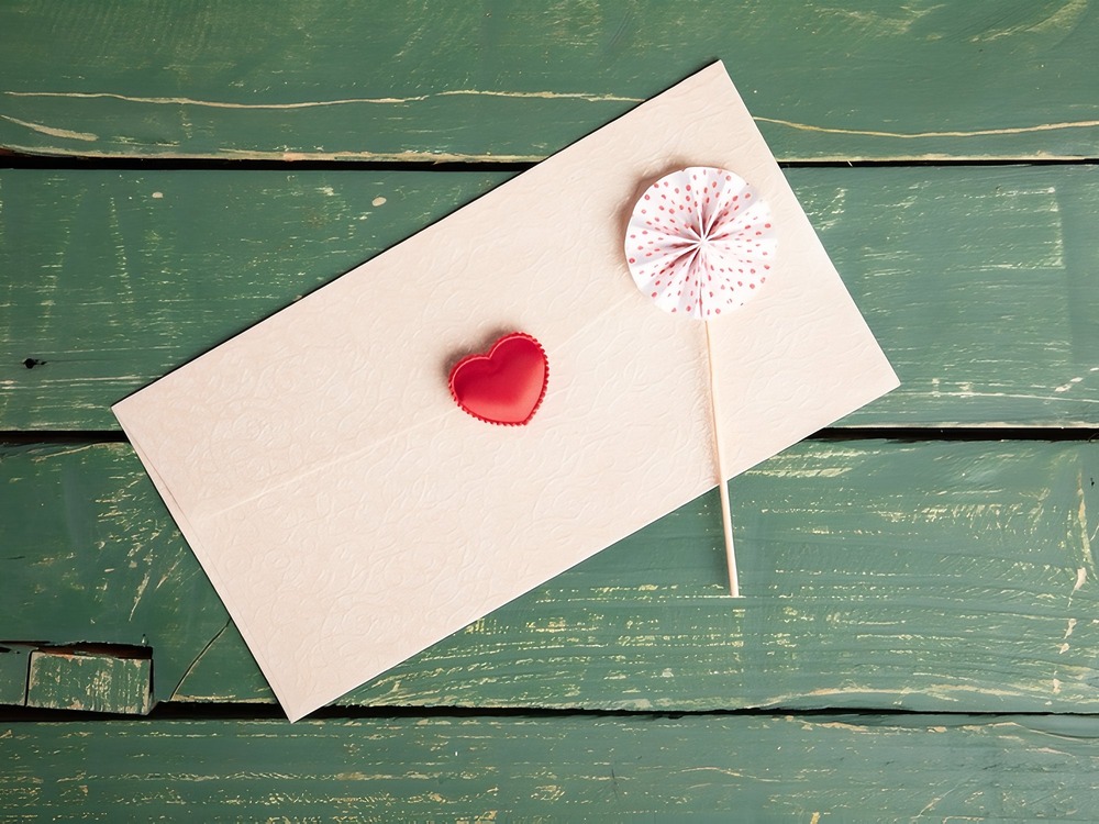 Cream envelope adorned with a red heart on green wood—an ideal touch for destination wedding website invitations.