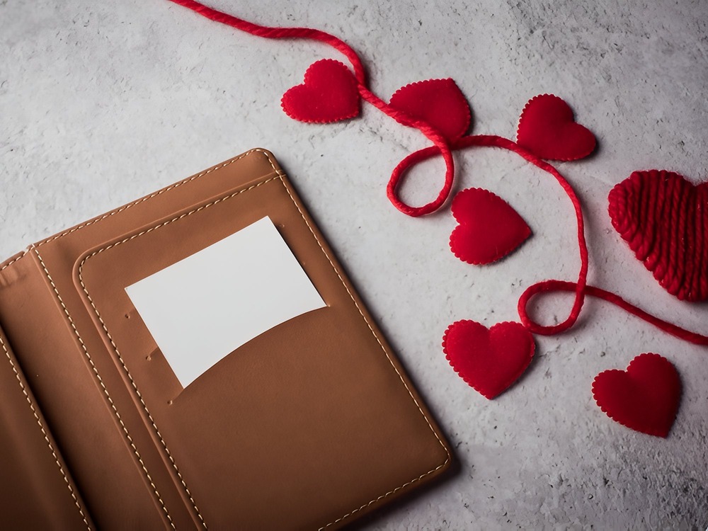 Brown wallet with blank card—perfect for destination wedding invitations or gifting—displayed beside charming felt hearts.