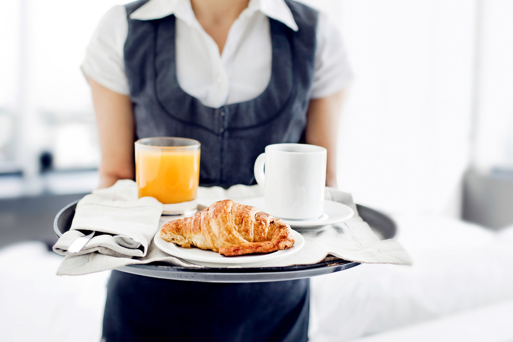 Concierge handing someone a tray with a croissant and orange juice