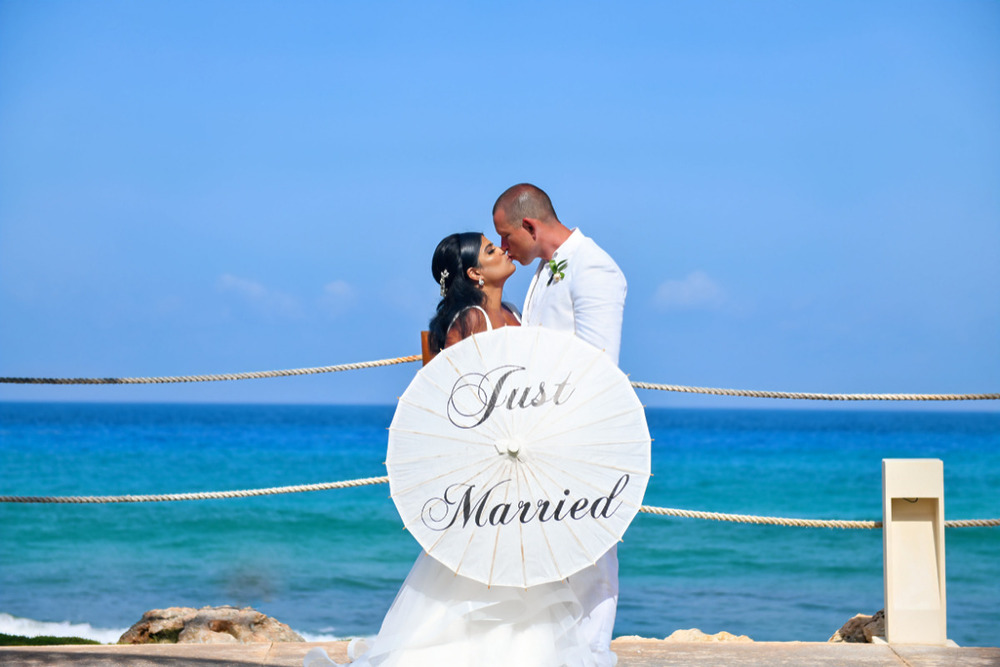 A bride and groom kissing in front of the ocean during their wedding.