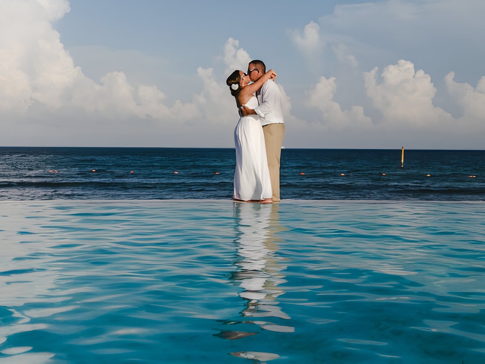 A couple dressed in white embraces by the ocean, dreaming about where to begin planning their perfect destination wedding.