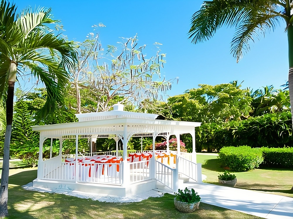 A white gazebo adorned with ribbons graces a lush tropical garden, offering the perfect starting point for planning a dream destination wedding.