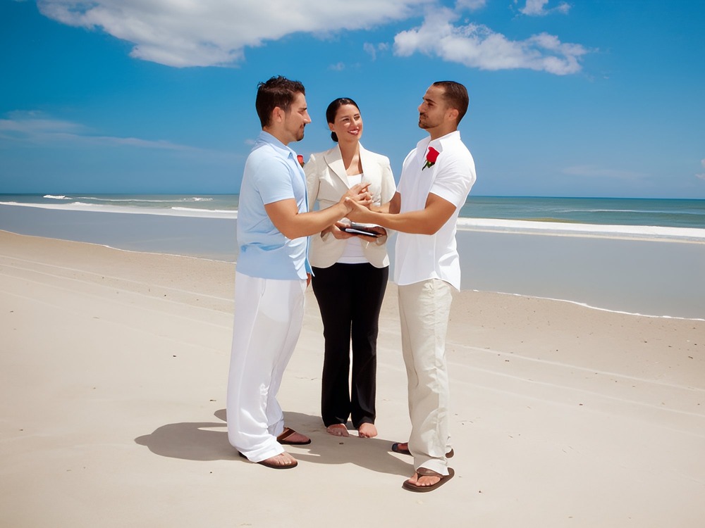 Two men exchange heartfelt vows during a beautiful LGBTQ+ destination wedding on the beach beneath a clear blue sky.