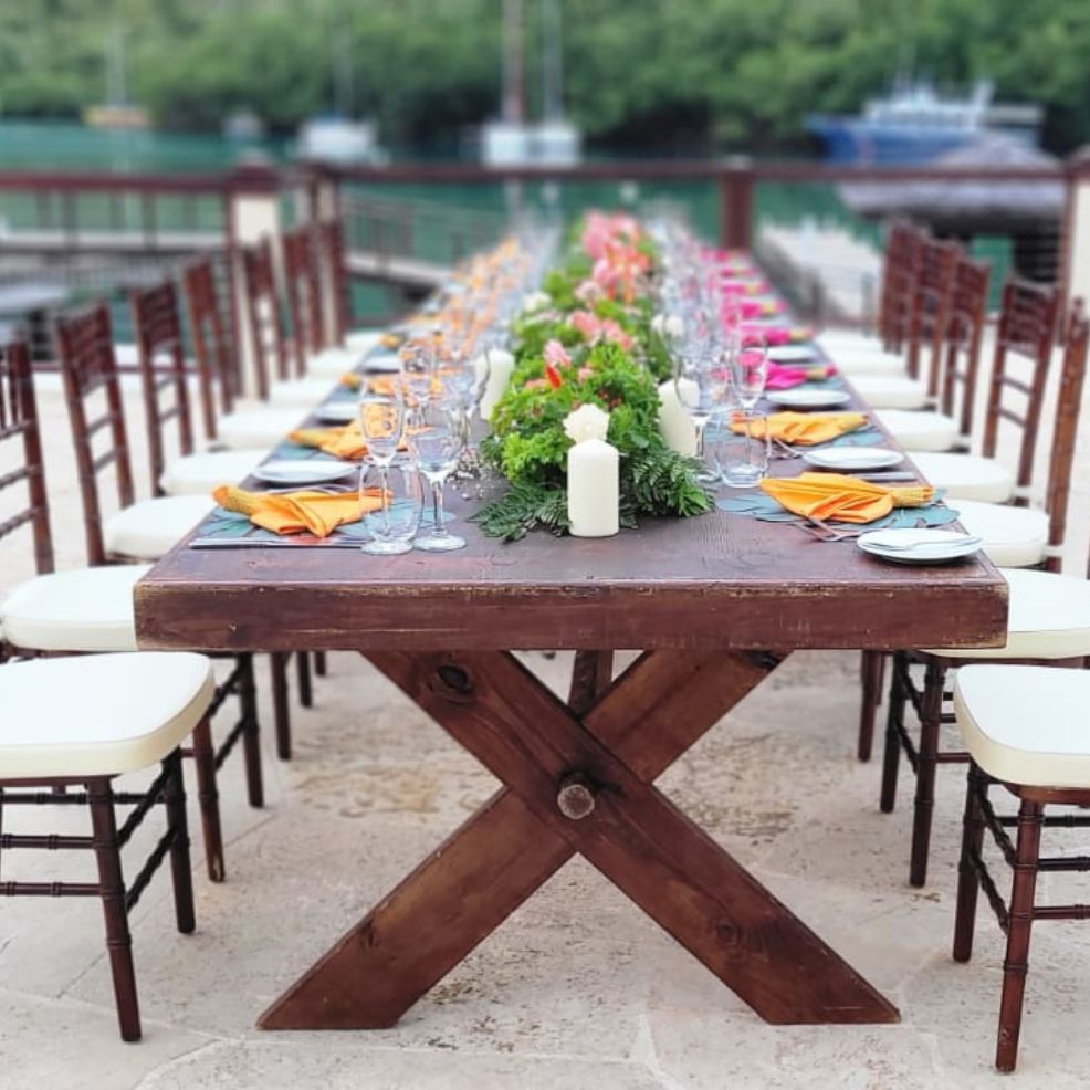 A long outdoor wedding dining table adorned with colorful napkins, glassware, and a floral centerpiece.
