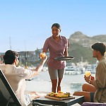 A server hands drinks to two guests by a marina—a beautiful setting for learning proper wedding or destination wedding tipping etiquette.