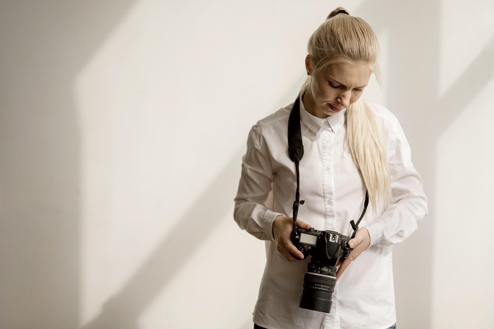 A person in a white shirt looks down, adjusting a camera in preparation for destination wedding photography.