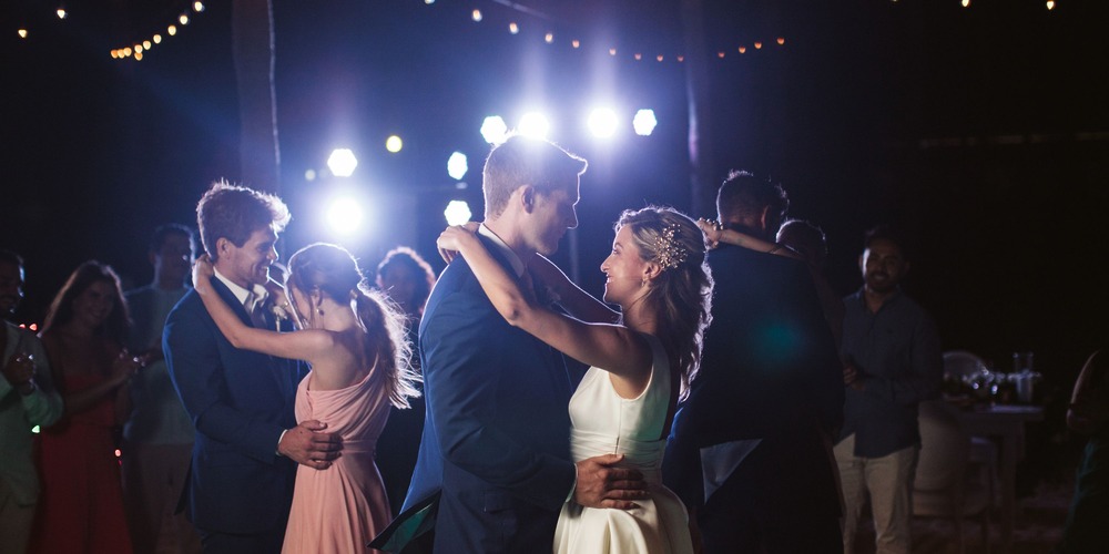 Couples sway together under glowing string lights, dancing to romantic music at an evening destination wedding.
