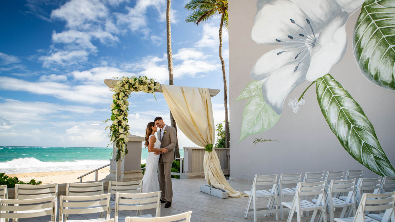 A bride and groom standing in front of the San Juan Marriott and Stellaris Casino on the beach.
