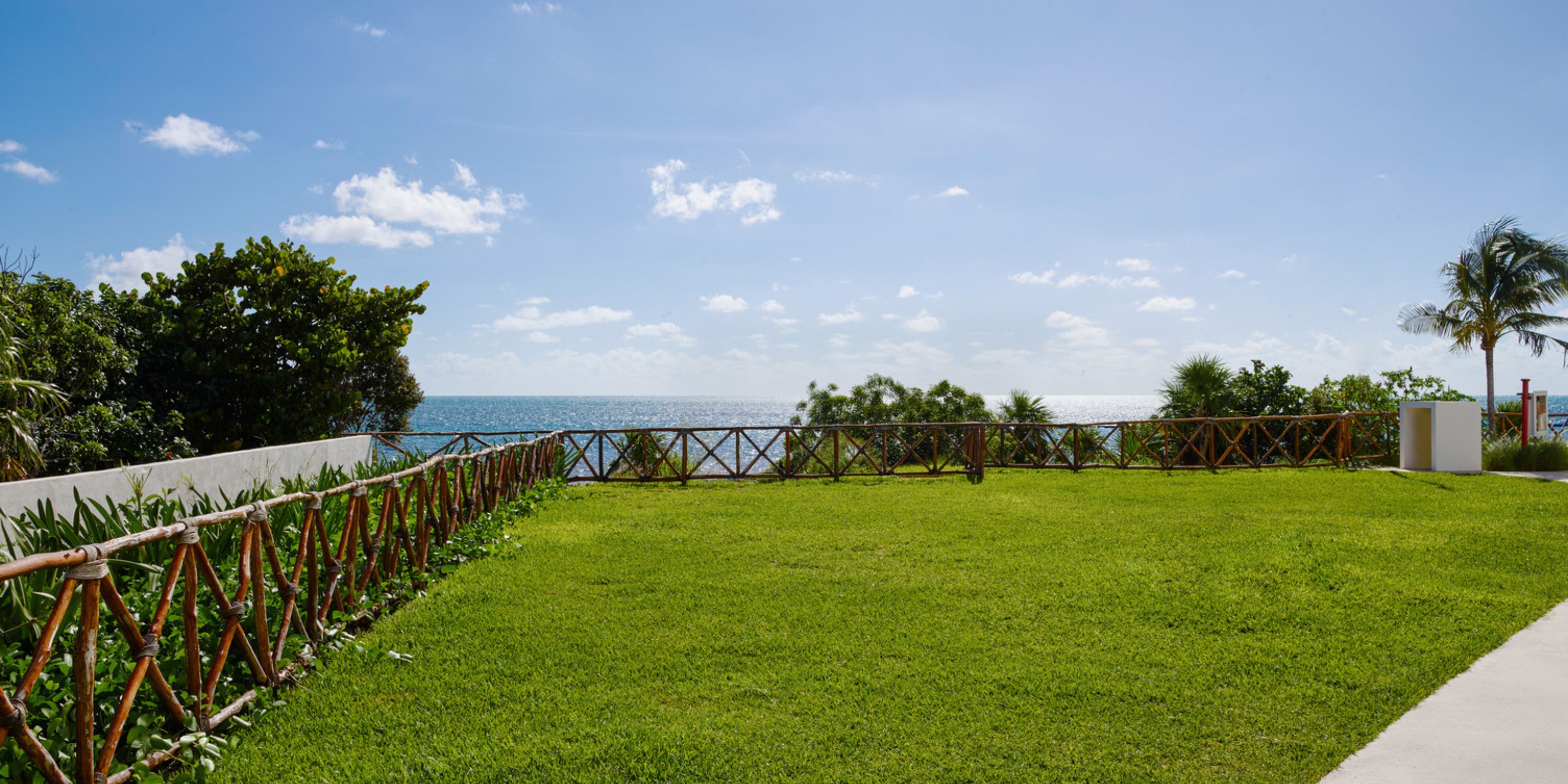 AVA Resort Cancun, a destination wedding spot with ocean views, green lawn, fence, and blue sky.