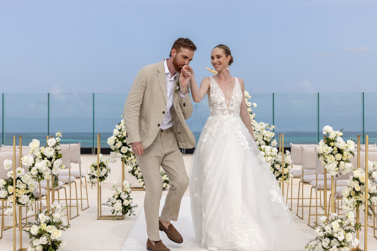 The bride and groom stroll hand-in-hand down the aisle, beautifully adorned with white flowers, at AVA Resort Cancun's stunning destination wedding.