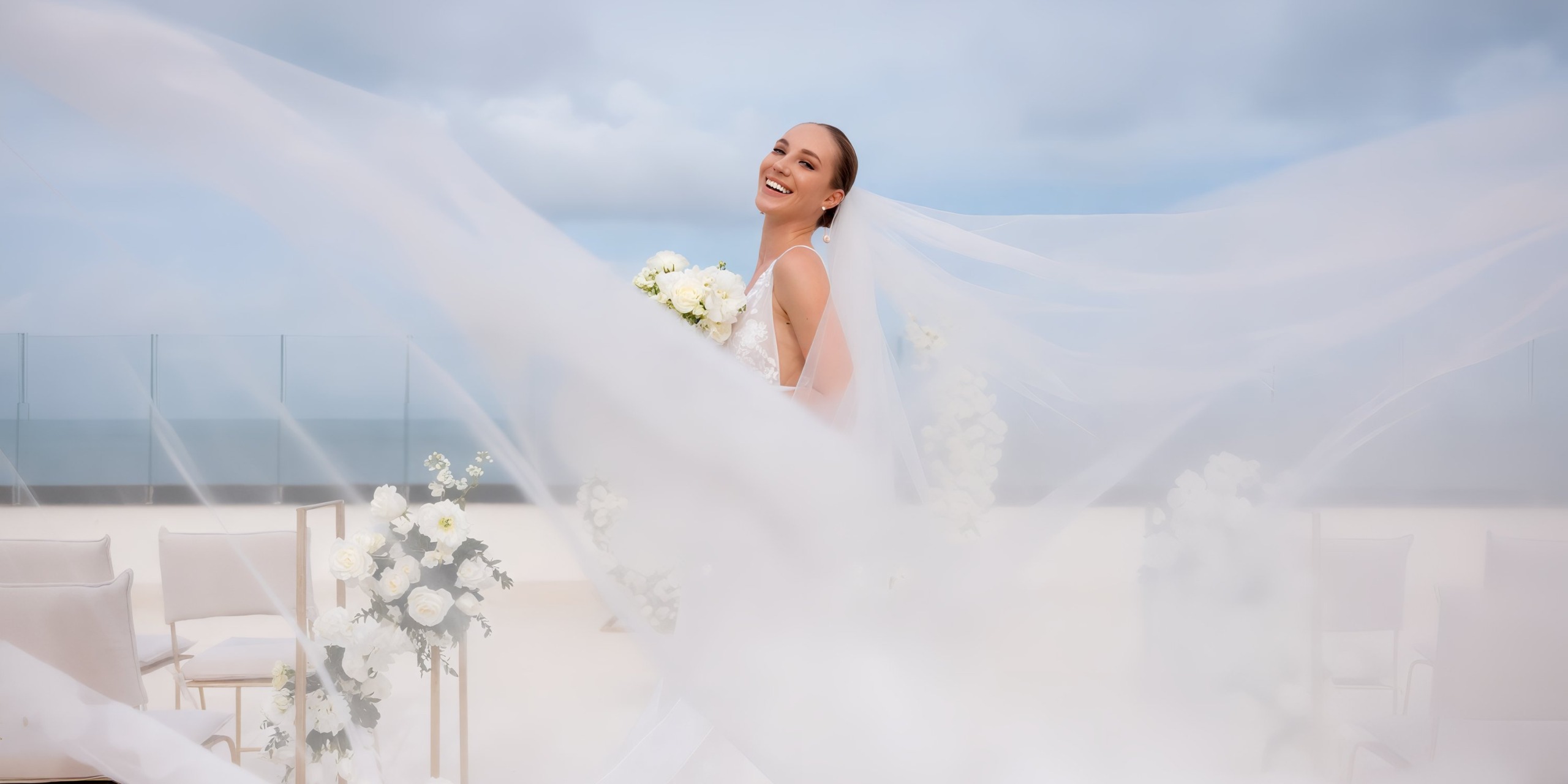 A bride, her veil flowing gracefully, holds a bouquet at the picturesque AVA Resort Cancun, with the beautiful beach providing the perfect backdrop for her destination wedding.