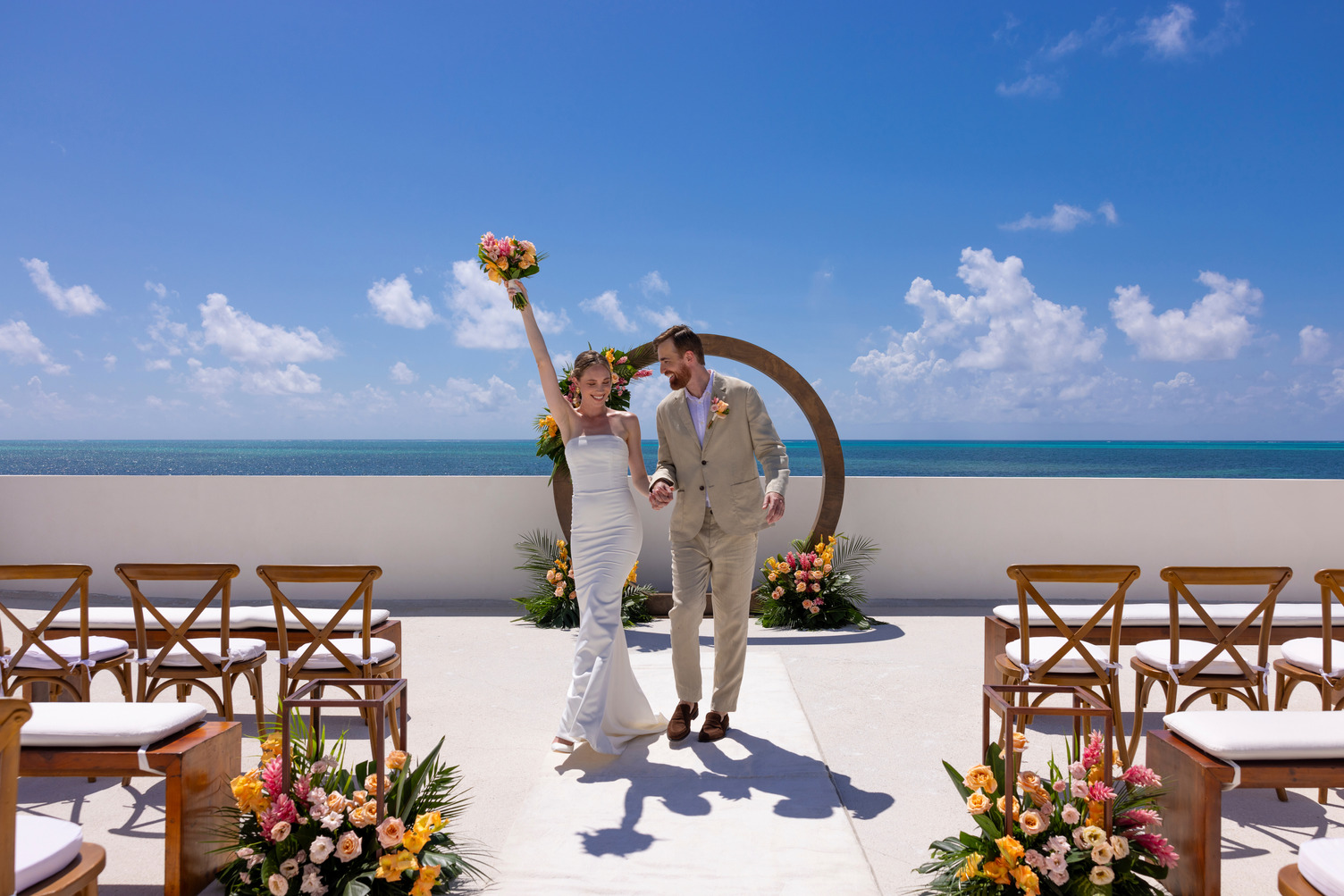 A couple celebrates their destination wedding on AVA Resort Cancun's seaside aisle beneath a clear blue sky.