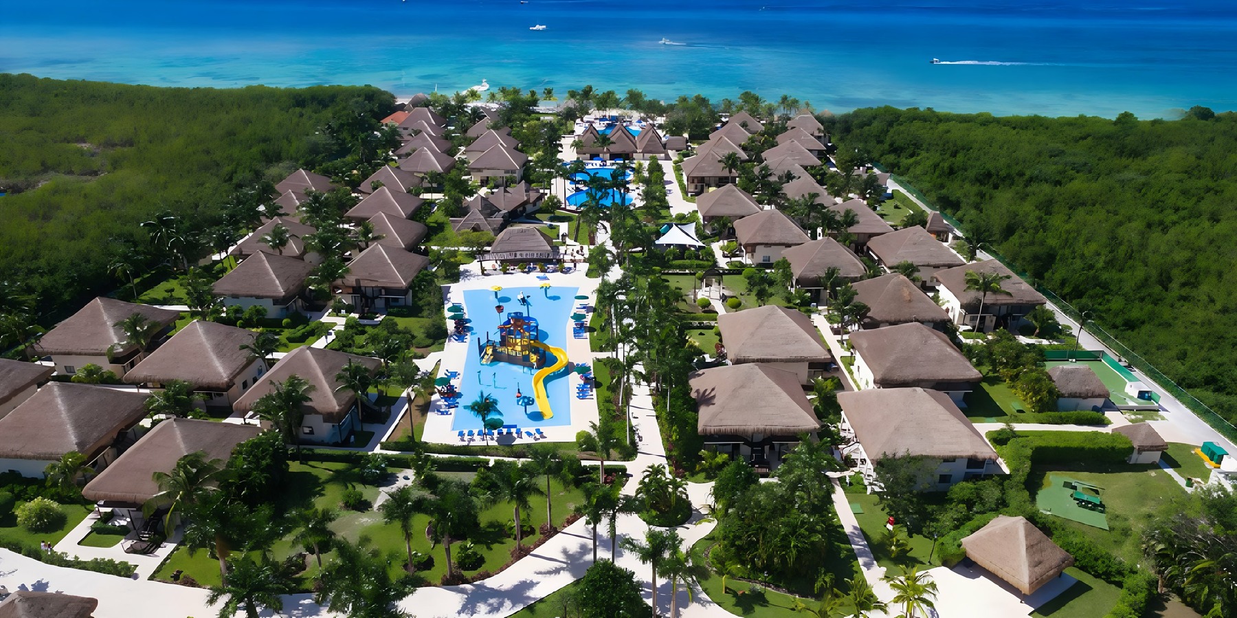 Aerial view of a tropical resort with thatched-roof buildings, swimming pools, and a beachfront setting.