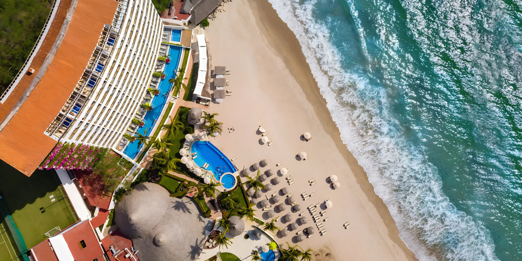 Aerial view of a beachside resort with a swimming pool and lounge chairs next to the turquoise ocean waves.