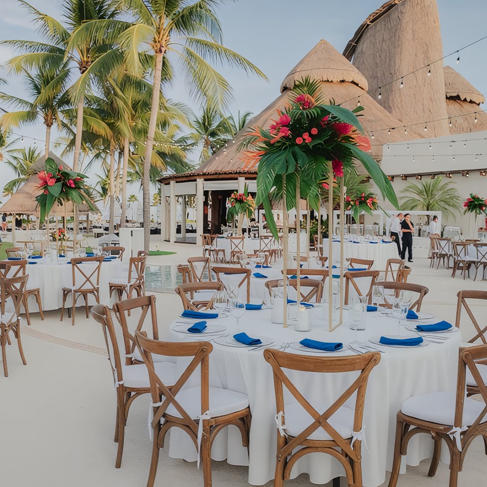 Destination wedding setup featuring round tables with white linens and vibrant tropical floral centerpieces.