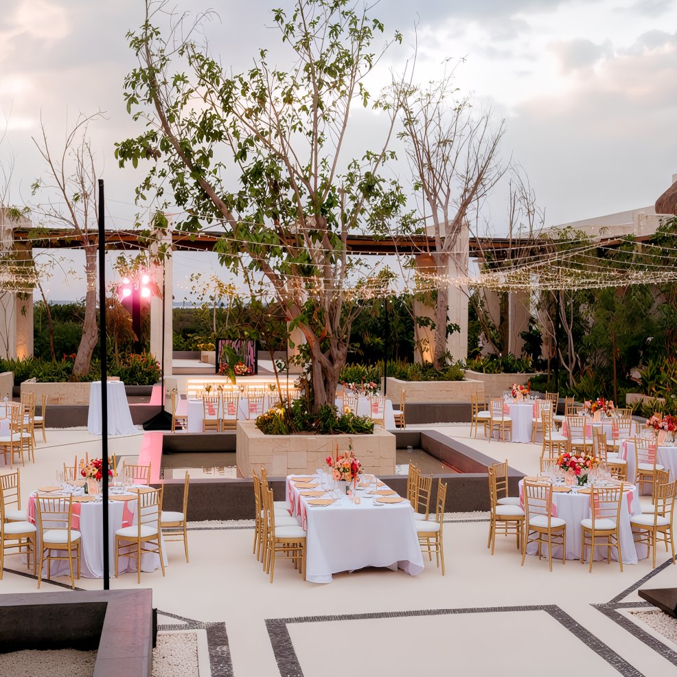 Destination wedding setup in a landscaped courtyard with decorated tables, gold chairs, and string lights.