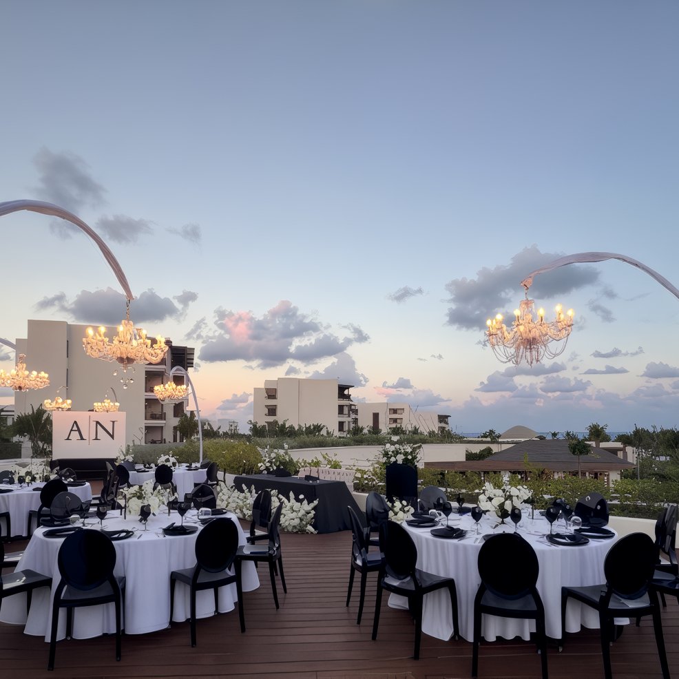 Destination wedding setup at dusk with round tables, black chairs, chandeliers, and floral centerpieces.