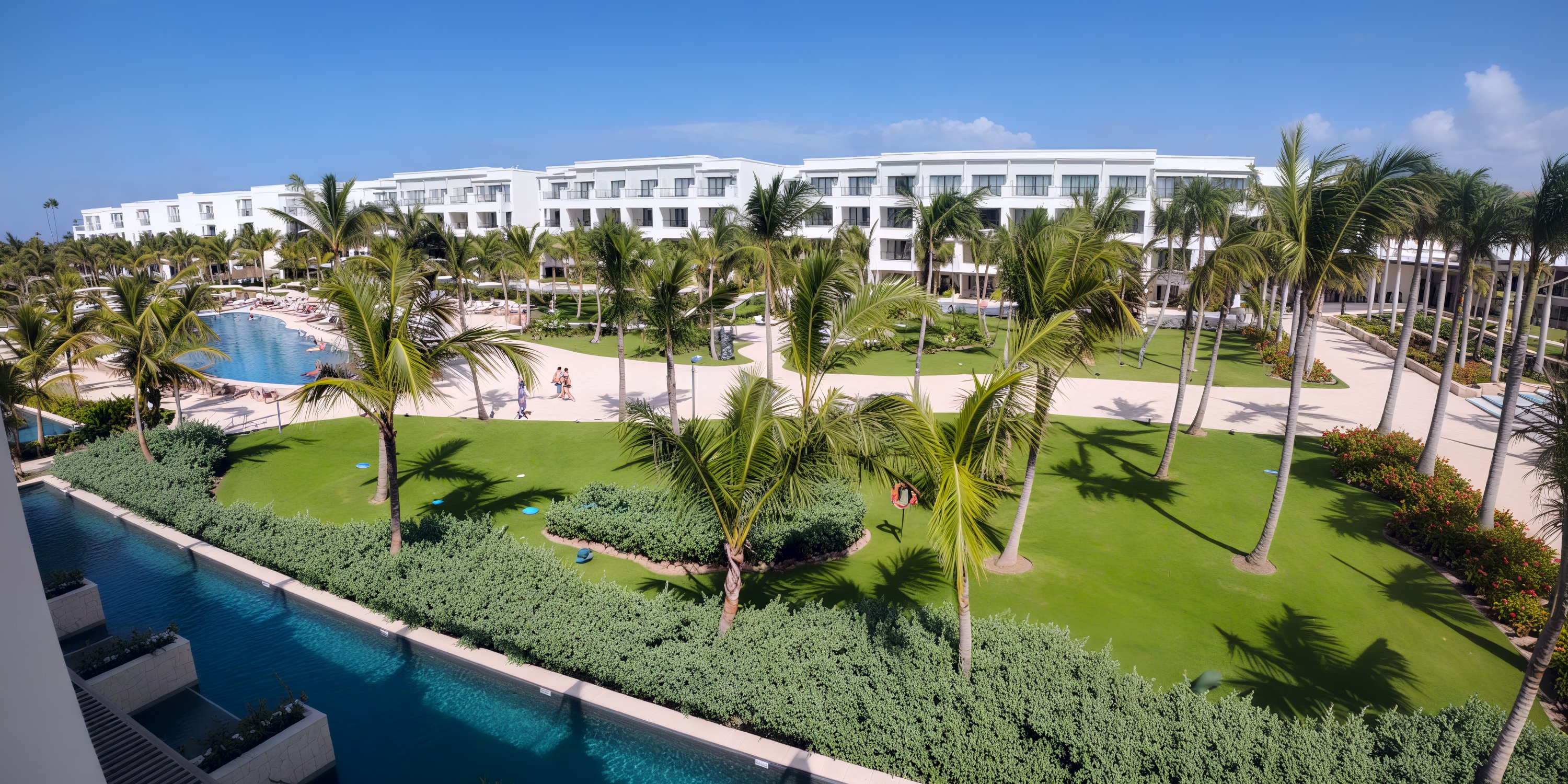 Secrets Tides: A modern destination wedding resort with palm trees, pools, lawns, and a blue sky.