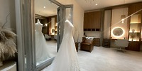 A Secrets Tides wedding gown is showcased on a mannequin in front of a large salon mirror.