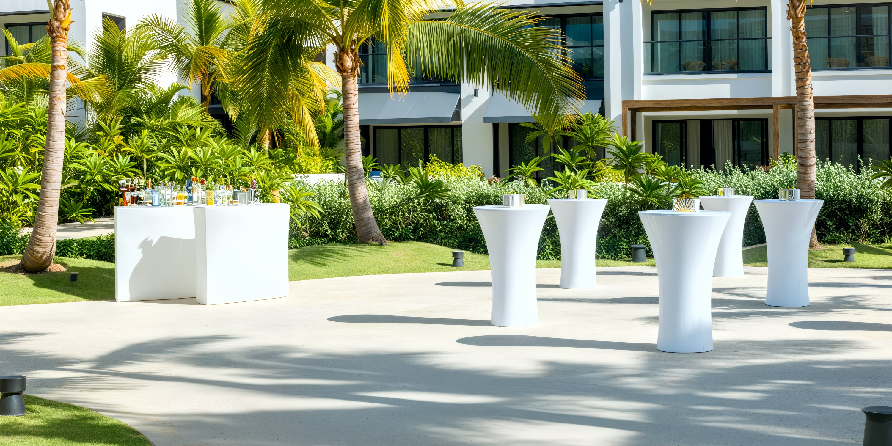 Secrets Tides destination wedding cocktail tables and bar set up outdoors, surrounded by palm trees and modern buildings.