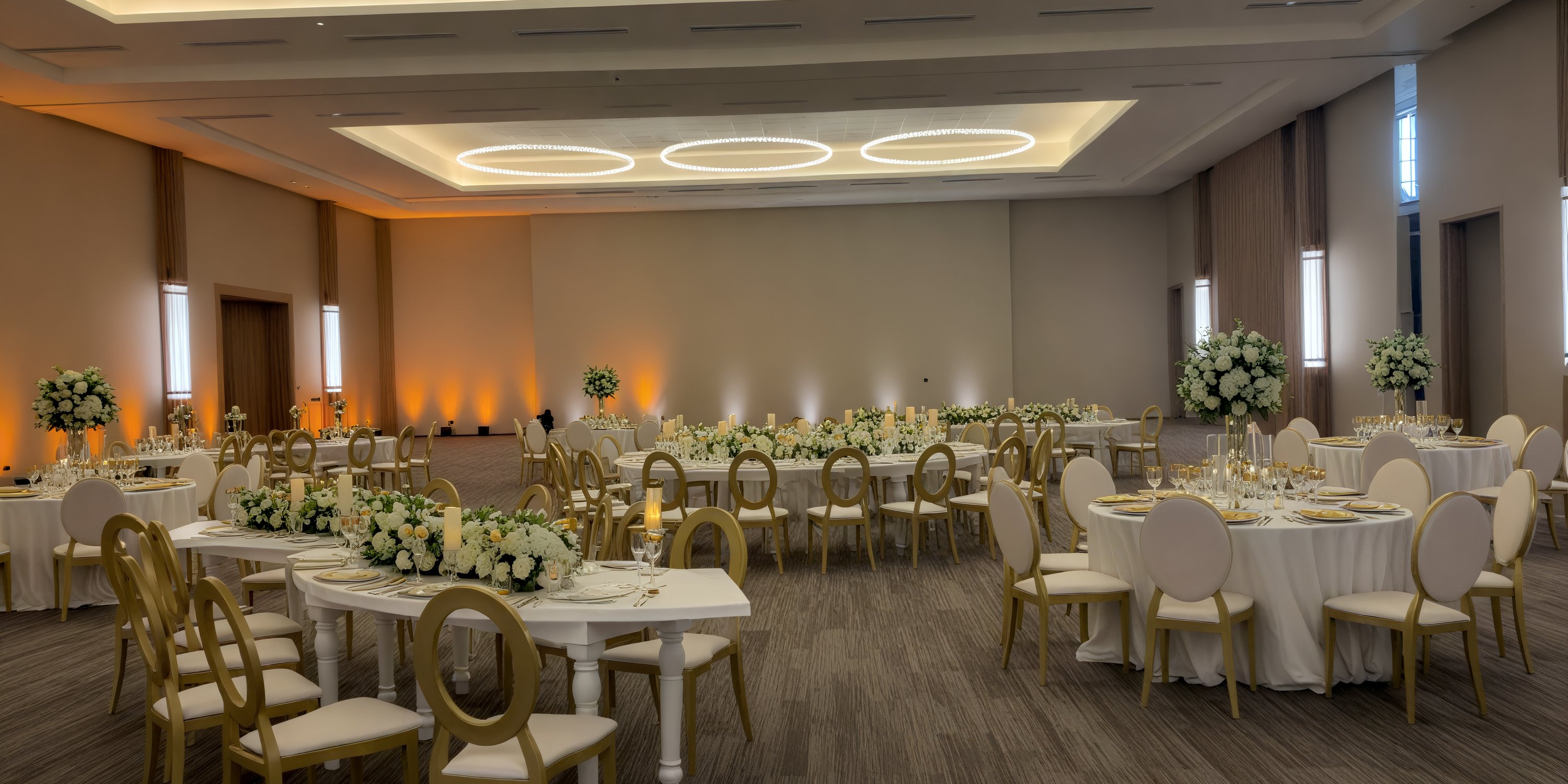 Secrets Tides banquet hall offers an elegant setting for your destination wedding, featuring round tables adorned with white linens and complemented by stylish gold chairs.