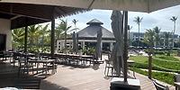 Secrets Tides outdoor dining set for a destination wedding, with empty tables, palm trees, and a thatched roof hut.