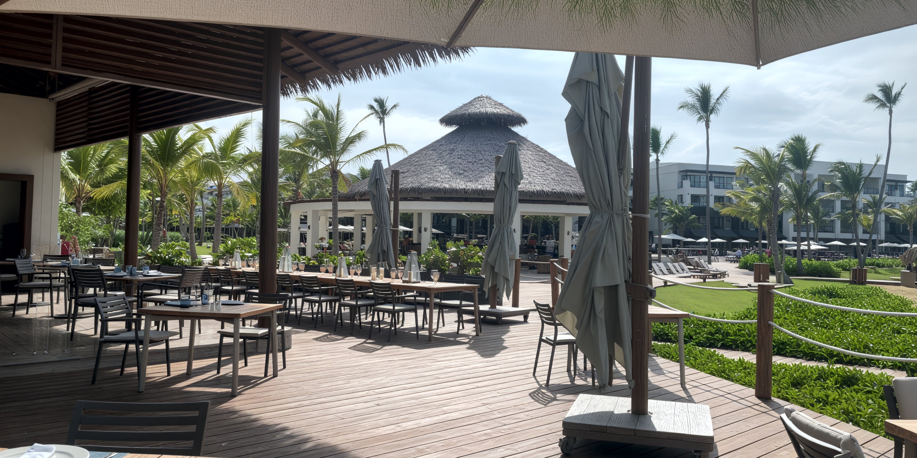Secrets Tides outdoor dining set for a destination wedding, with empty tables, palm trees, and a thatched roof hut.