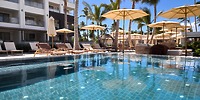 Poolside view with lounge chairs and umbrellas at Secrets Tides, perfect for a sunny destination wedding.