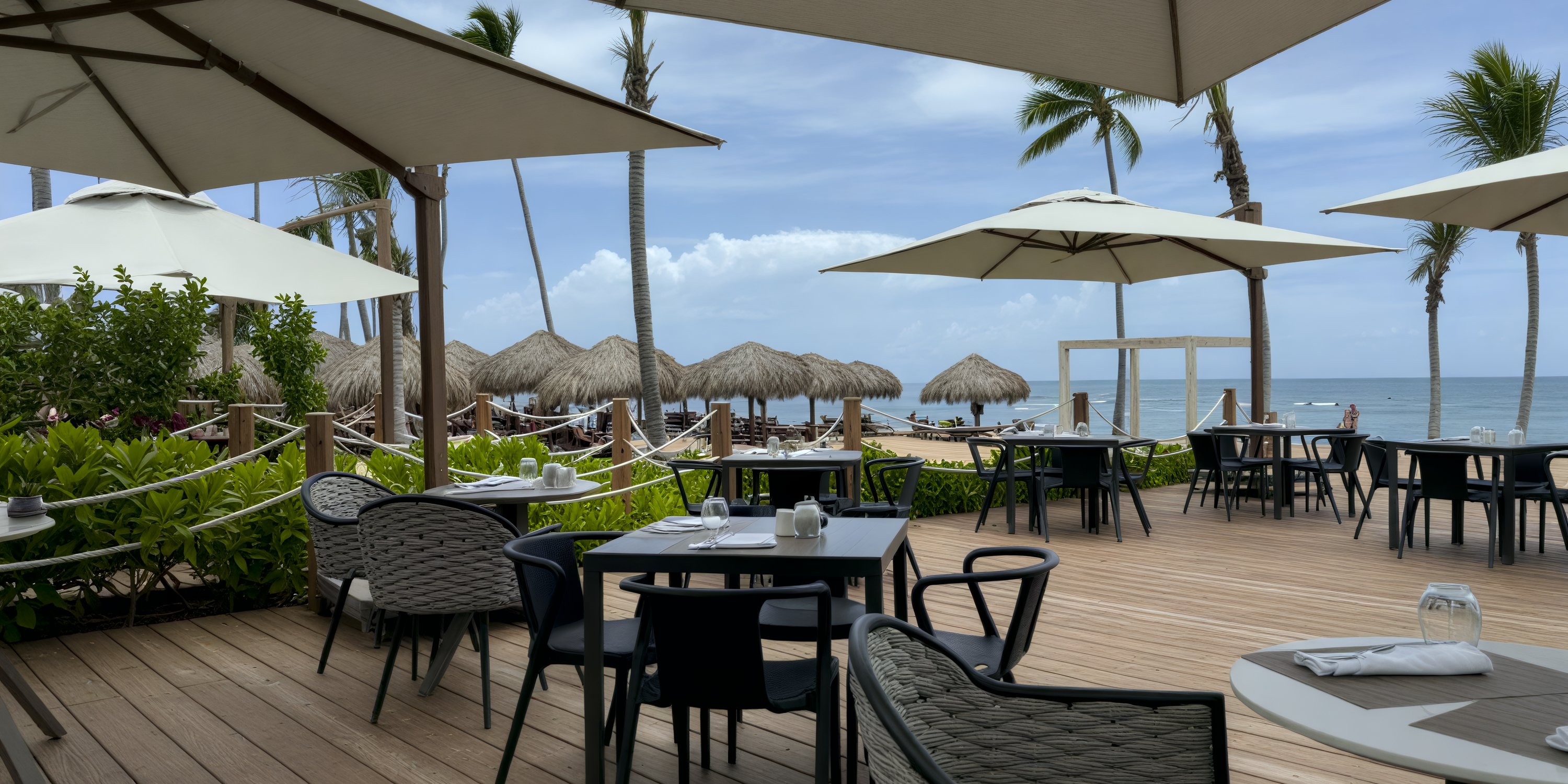 Secrets Tides features shaded tables on a wooden deck with ocean views, ideal for a destination wedding.