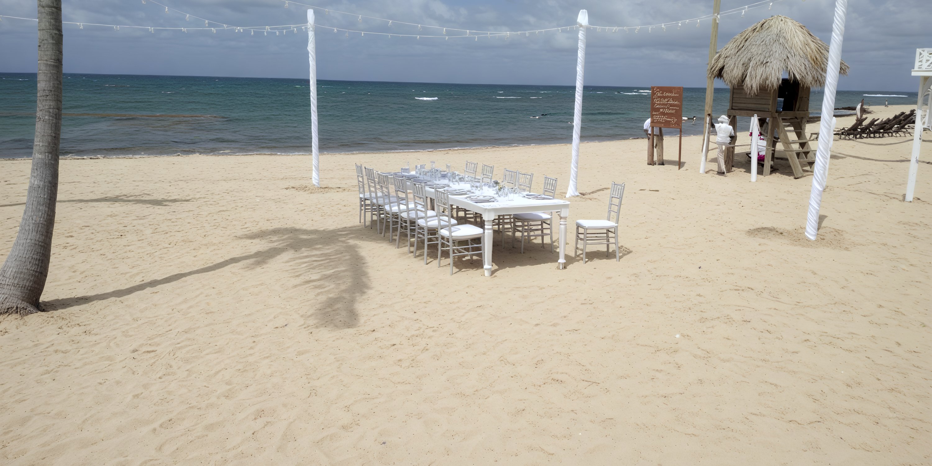 A Secrets Tides dining set is set for a destination wedding on a sandy beach under cloudy skies.