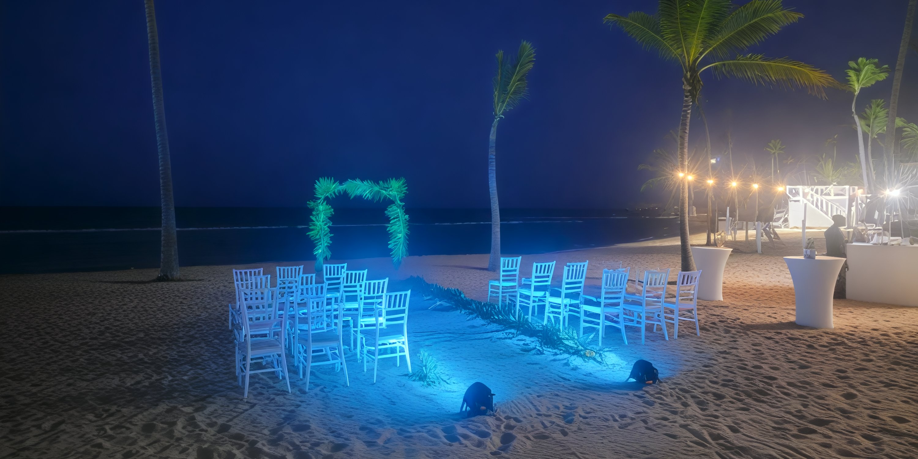 Secrets Tides destination wedding setup: white chairs, floral arch, and blue lighting illuminating the night.