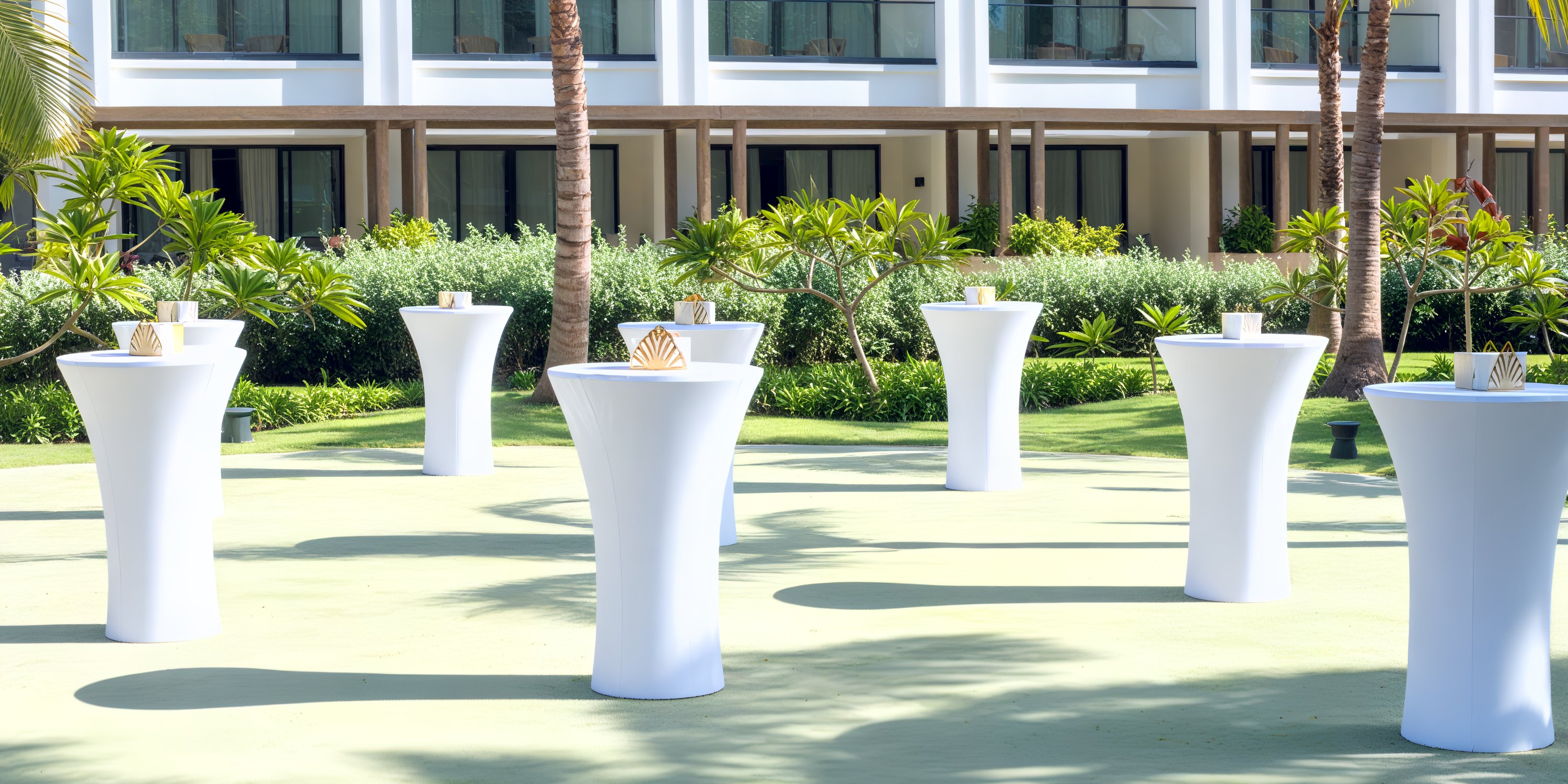 Secrets Tides cocktail tables with white covers set up for a destination wedding near modern architecture and greenery.