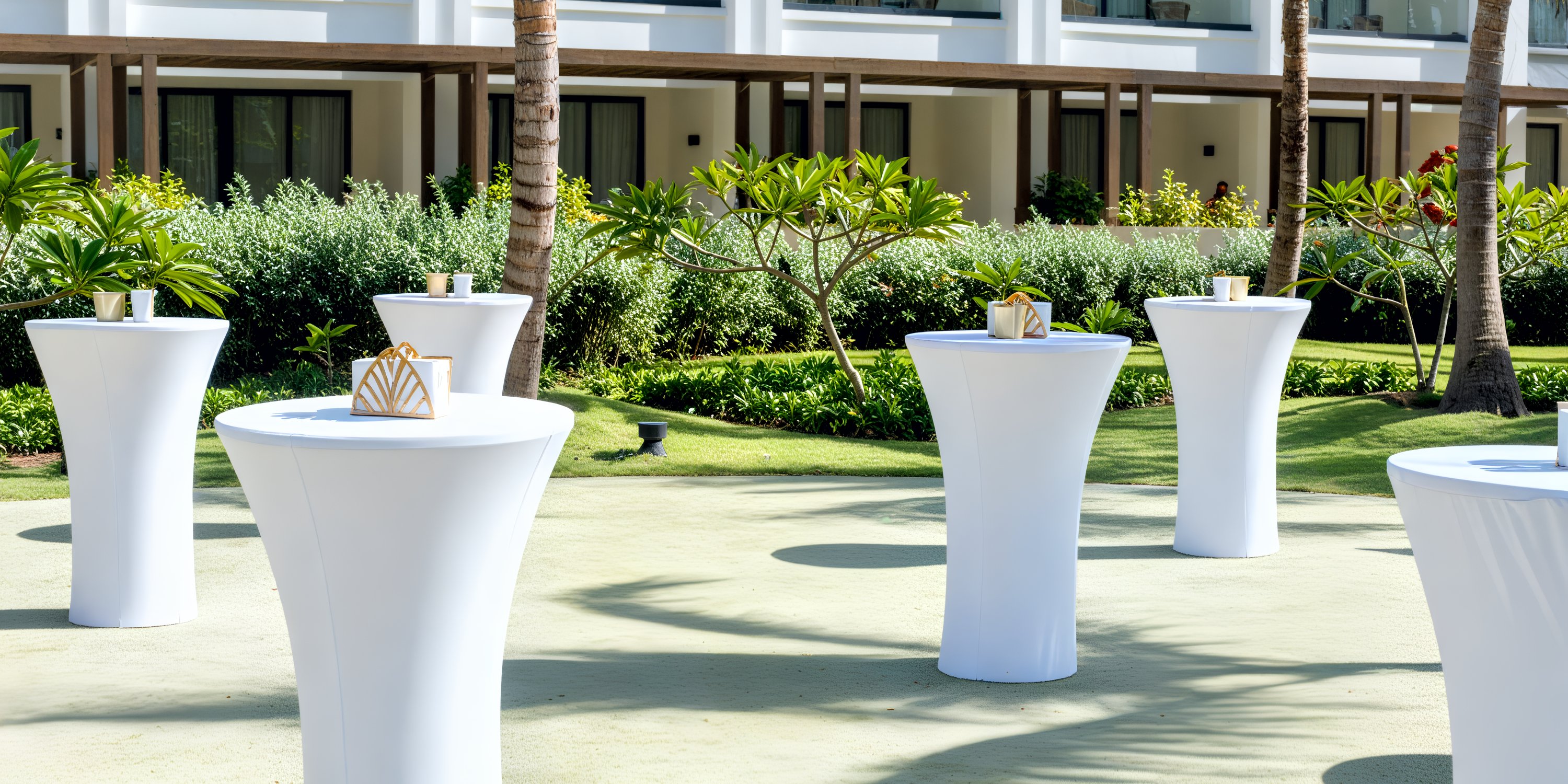 Destination wedding setup featuring Secrets Tides tall white cocktail tables and gold centerpieces outside.