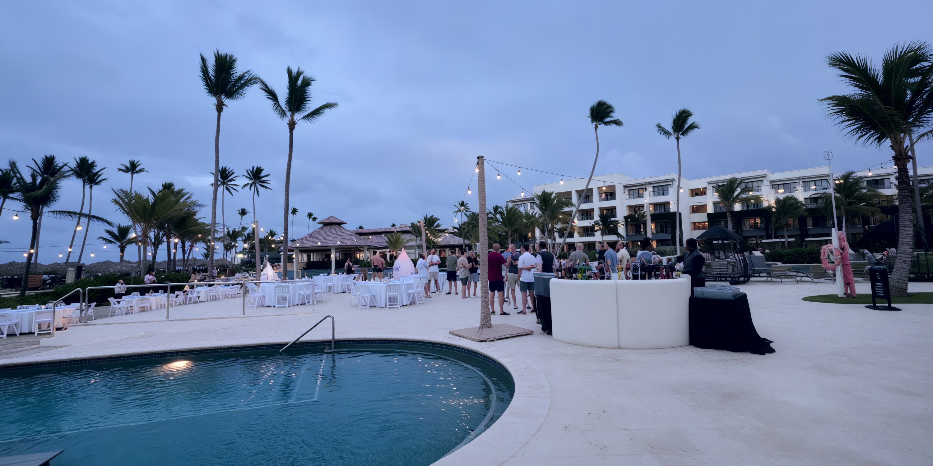 Guests attend a destination wedding by the pool, surrounded by tables and lights at Secrets Tides resort.