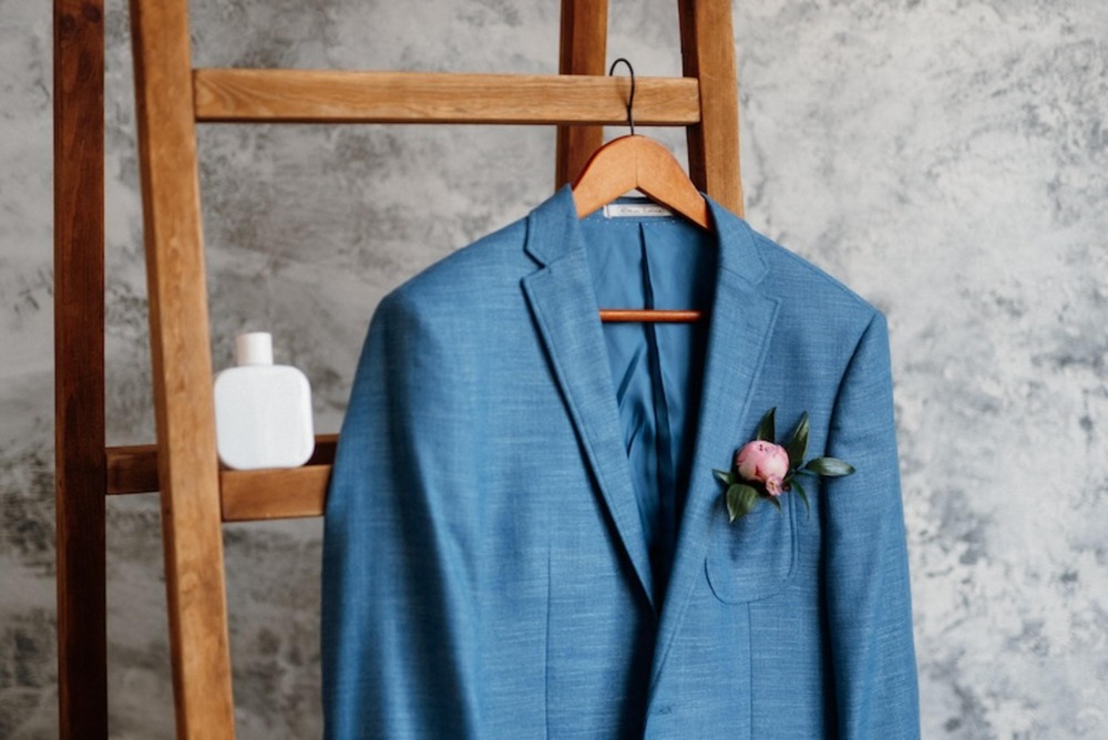 A blue suit jacket, perfect for a destination wedding, hangs on a ladder beside a white bottle—an ideal example for tips on packing wedding attire.