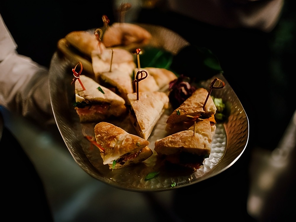 A plate of triangular sandwich wedges, perfect as an elegant appetizer for a wedding or destination wedding tasting event.