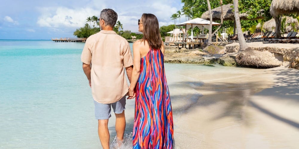 A couple strolls hand in hand along clear blue water on a tropical beach after their destination wedding.
