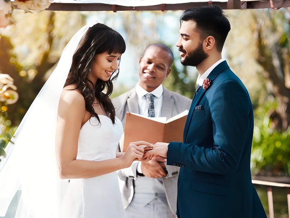 At their destination wedding ceremony, the bride and groom exchange rings and speak their traditional wedding vows outdoors.