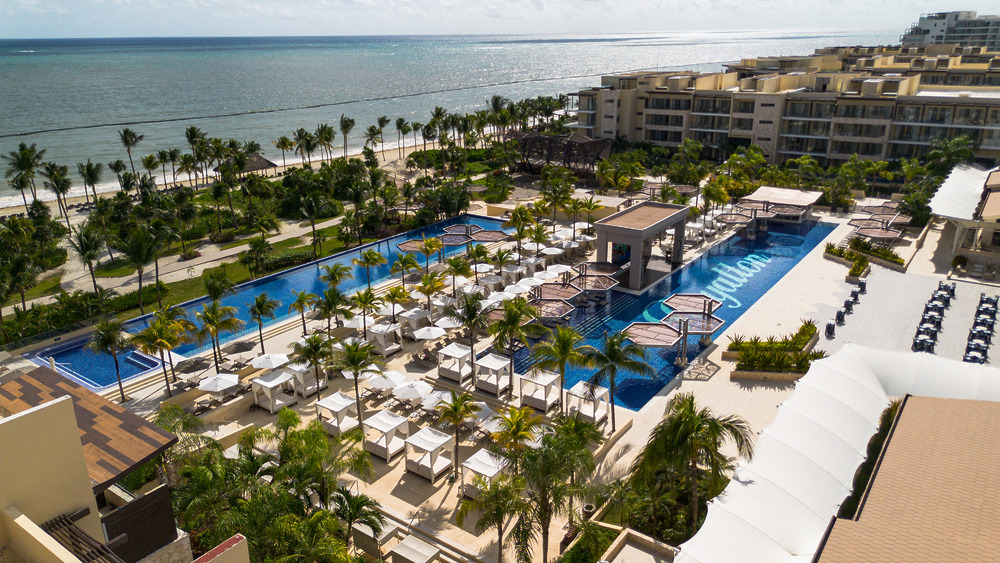 Aerial view of a beachfront resort, ideal for a destination wedding, with pools and palm trees by the ocean.