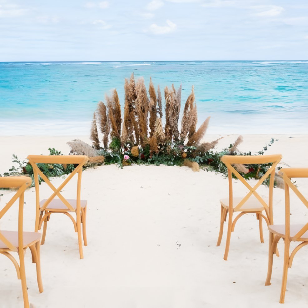 Wooden chairs arranged for a destination wedding on the beach, facing the ocean with pampas grass d&eacute;cor.
